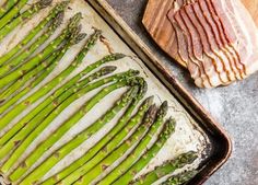 asparagus on a baking sheet ready to go into the oven with bacon in the background