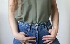 a woman with her hands on her hips wearing high waisted jeans and a green shirt