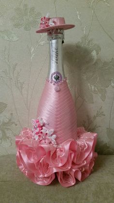 a pink hat on top of a wine bottle with flowers and ribbons around the bottom