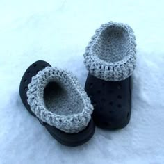 two pairs of black slippers sitting on top of snow covered ground with crocheted trim