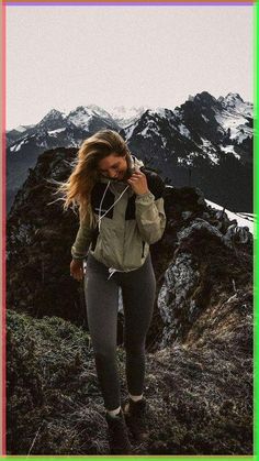 a woman standing on top of a mountain while listening to music with headphones in her ears