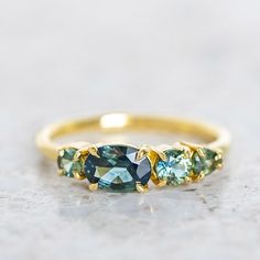 Our Splice Ring has been set with shades of brilliant cut green sapphires. Brilliant cut oval sapphire in centre measures 7x5mm. Band width 1.8mm. Gold weight in 14ct 3.1g approx. Pictured with a high shine finish. Please note, we will match the sapphires as close to the image as possible, but each stone is unique and may vary in appearance and colour from what is depicted on the site.