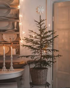 a small christmas tree in a wicker basket next to a dining room table with dishes on it