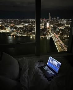 an open laptop computer sitting on top of a bed in front of a large window