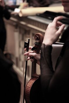 a woman holding a violin in her right hand and looking at the back of it