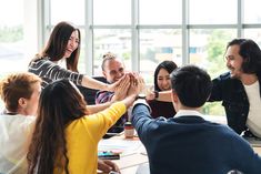 a group of people sitting around a table with their hands together