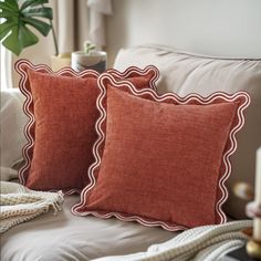 two red pillows sitting on top of a bed next to a plant in a vase