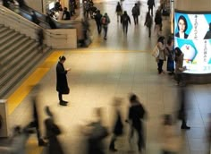 many people are walking around in the subway station and one is using his cell phone