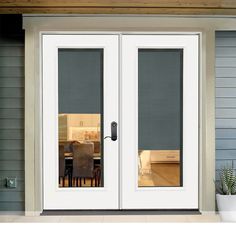 a white double door with sidelights and blinds on the outside of it, in front of a house