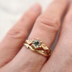 "Handcrafted from a delicate budded twig, the Flora Solitaire Band is adorned with thyme leaves and features a mint green Montana Sapphire in a 6-prong setting.  100% recycled gold  100% ethically-sourced Montana Sapphire Every single ring in my collection is designed, sculpted and produced entirely by hand. I never use computers and I never use \"off-the-shelf\" designs that you see in so many jewelry stores. Each ring begins by casting an actual twig or piece of bark; its natural, imperfectly Leaf Engagement Ring Nature, Engagement Rings Organic, Stacked Engagement And Wedding Rings, Leaf Rings, Green Montana, Contour Ring, Solitaire Bands, Nature Engagement Ring, Montana Sapphire Ring