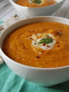 a white bowl filled with carrot soup on top of a green table cloth next to a spoon