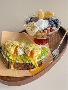 an open faced sandwich on a wooden tray next to a bowl of fruit and yogurt