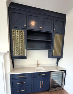 an empty kitchen with blue cabinets and white counter tops, including a wine cooler in the corner