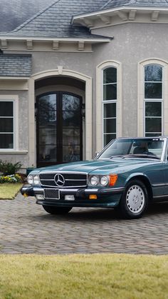 a mercedes benz is parked in front of a large house with two doors and windows