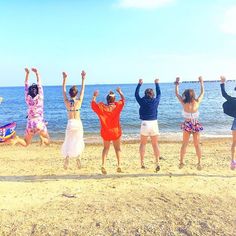 four people jumping in the air on a beach with their arms up and hands raised