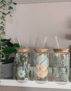 three mason jars with floral designs and straws are sitting on a shelf next to a potted plant