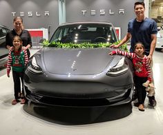 three children and an adult standing next to a tesla car