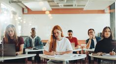 group of students sitting at desks in classroom with laptops and notebooks on their laps