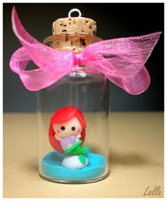 a little mermaid under a glass bottle with a pink bow