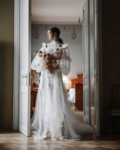 a woman in a wedding dress is standing near an open door and holding a bouquet