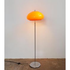 an orange floor lamp on a white wall