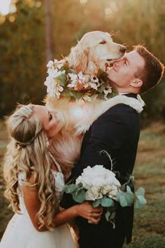 a bride and groom kissing their dog in front of the sun shining through the trees