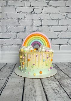 a rainbow cake with white frosting and sprinkles on the top is sitting on a wooden table