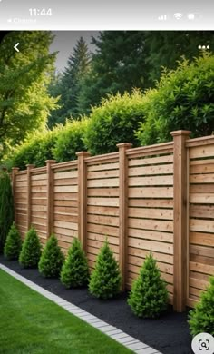 a wooden fence in the middle of a yard with trees and bushes on either side