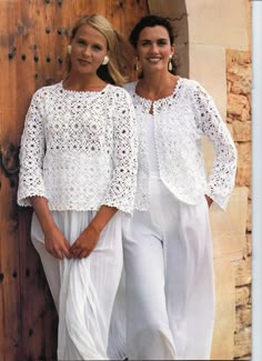 two women standing next to each other in front of a wooden wall wearing white clothing