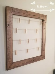 a wooden frame hanging on the wall with clothes pins attached to it and a white background