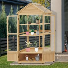 a small wooden greenhouse with potted plants on the shelves in front of a house