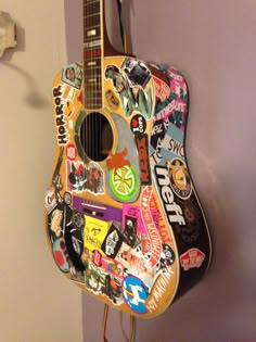 an acoustic guitar covered in stickers and magnets hangs on the wall next to a cord