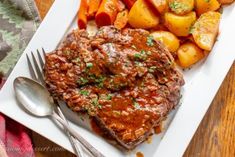 a white plate topped with meat, potatoes and carrots next to a fork on a wooden table