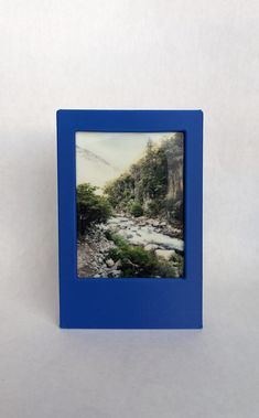 a small blue frame with a river in the middle and trees on both sides, against a white background