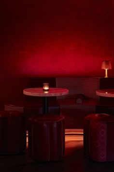 two tables and stools in a room with red lighting on the wall behind them