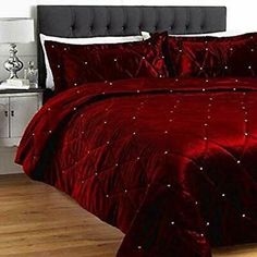 a bed with red comforter and pillows on top of wooden floor next to white wall