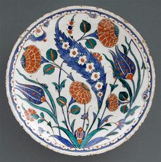 a white and blue plate with orange flowers on the bottom, surrounded by green leaves