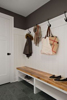 a bench with two coats hanging on the hooks and one bag sitting on top of it