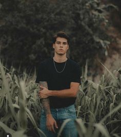 a man standing in the middle of a corn field with his arms crossed and looking off into the distance