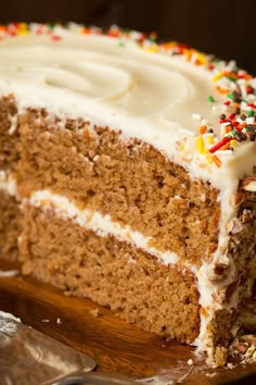 a piece of cake with white frosting and sprinkles on top is sitting on a wooden platter