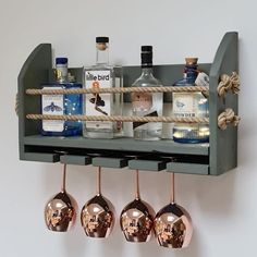 three wine glasses hanging from a shelf with liquor bottles on the top and two copper goblets below