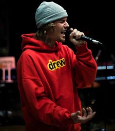 a man in a red hoodie singing into a microphone