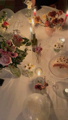 a white table topped with lots of plates covered in cake and flowers next to candles