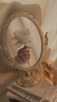 a person holding a flower in front of a mirror on top of books and jewelry