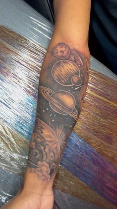 a person's arm with tattoos on it and saturn in the sky above them