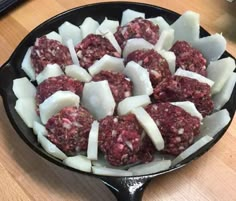 a skillet filled with meatballs and cheeses on top of a wooden table