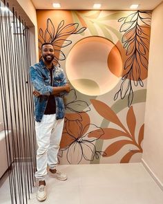 a man standing in front of a wall with flowers painted on it and an artistic mural behind him