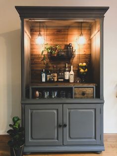 an entertainment center with liquor bottles and glasses on the top, in front of a wood paneled wall