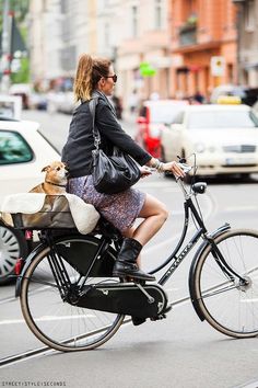 a woman riding a bike with a pink basket on the front and back wheel, in an urban setting