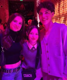 three people standing next to each other in front of a brick wall with neon lights